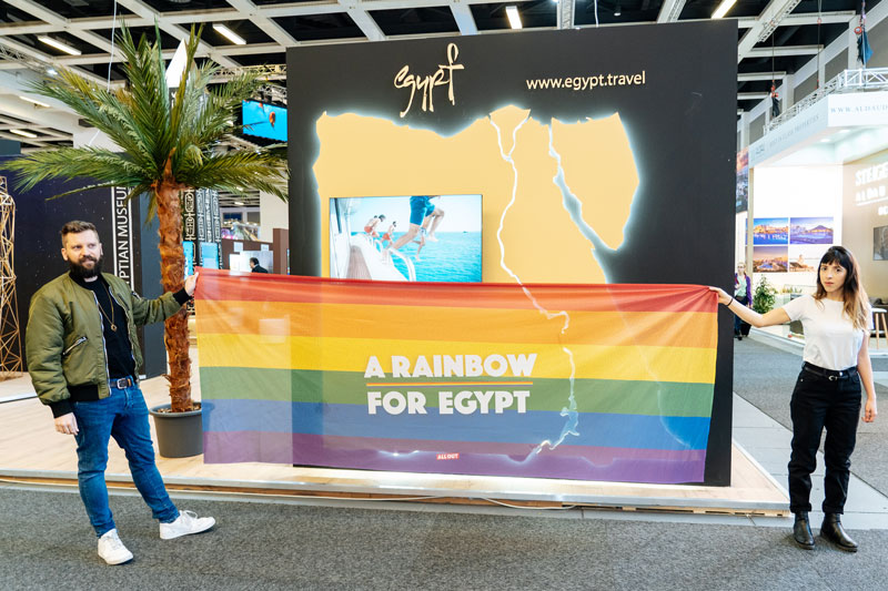 Ativistas da All Out seguram a bandeira do arco íris em frente ao estande do Egito na feira.